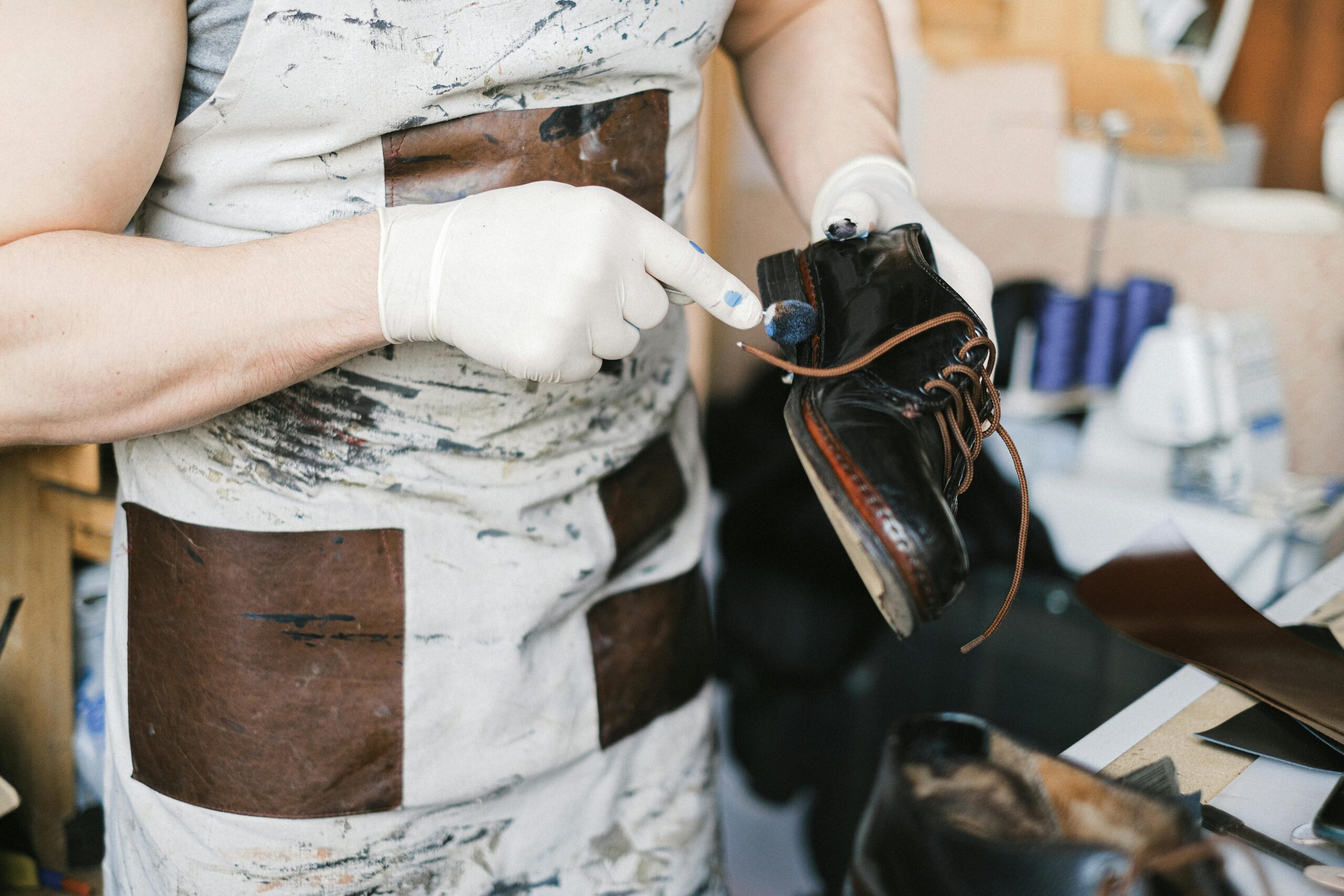 A craftsman polishing black leather shoes with gloves in a workshop setting.